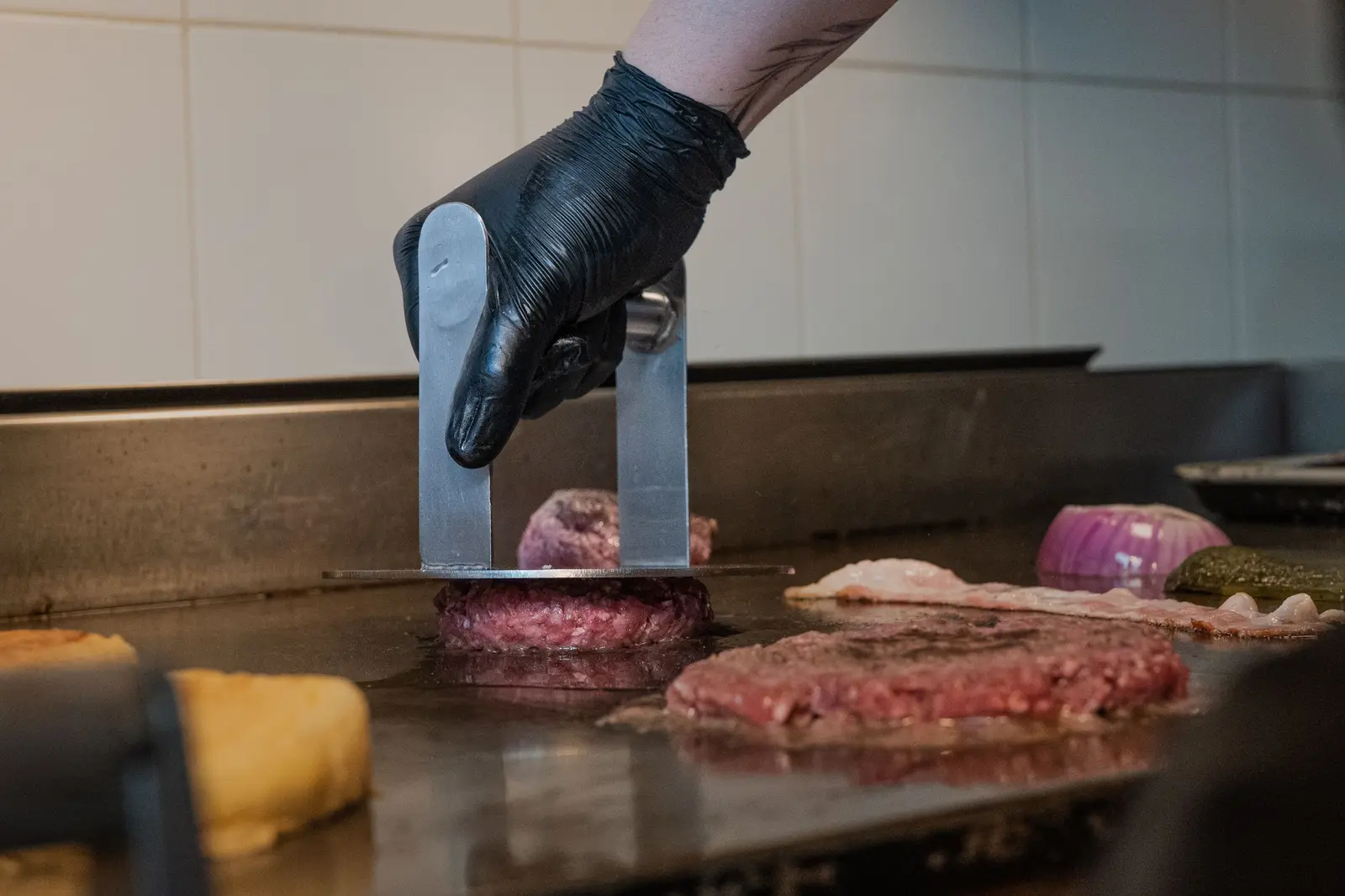 Cook pressing a patty flat on the griddle with a smasher